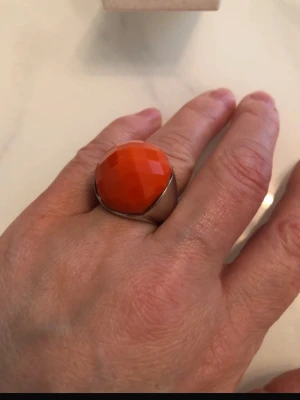 Statementring med orange sten - Säljer en chunky statementring med stor, facettslipad orange sten och bred, silvrig ringbas. Ringen har en modern och edgy vibe som verkligen drar blickarna till sig. Perfekt för dig som vill sticka ut och addera färg till din look.