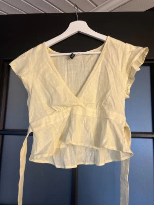 Croppad topp från hm - Säljer denna söta toppen från hm, den är ljusgul, croppad, med snören som man kan knyta antingen fram eller bak🌼