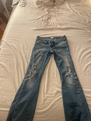 Blå bootcut jeans med hål - Säljer dessa blå lowaist bootcut jeans ifrån Gina. Jag säljer dessa för att dom blivit förkorta och att hålen blivit större än vad dom va när jag köpte dom