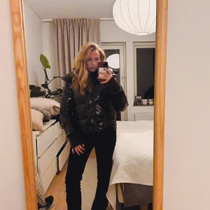 Svart pufferjacka från Calvin Klein - Säljer en svart, glansig pufferjacka från Calvin Klein med huva och dragkedja framtill. Jackan har en schysst oversized passform och är perfekt för kalla dagar. Diskret logga på bröstet och quiltad design som ger extra volym och stil.har inga defekter.