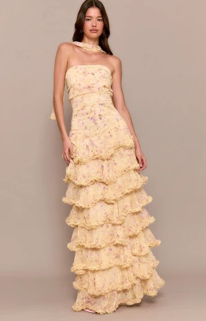 Blommig långklänning med volanger - Drömmig ljusgul långklänning från PLT med blommigt mönster i lila och rosa. Klänningen är axelbandslös med tillhörande ”sjal” och har flera lager volanger hela vägen ner. Använd 1 gång, som ny.