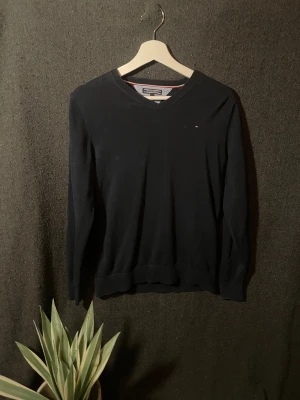 Svart v-ringad tröja Tommy Hilfiger - Klassisk svart v-ringad tröja från Tommy Hilfiger med diskret logga på bröstet. Tröjan är långärmad och har ribbade muddar vid ärmslut och nederkant. Perfekt för lager-på-lager och enkel att matcha med allt.