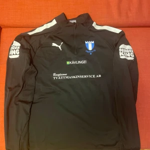 Svart långärmad träningströja Malmö ff - Svart långärmad träningströja från Malmö FF. Tröjan har vita detaljer på axlarna, halv dragkedja. Tröjan är i nyskick. 