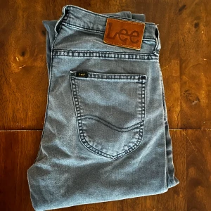  Lee Luke jeans W29 L32 - Snygga grå/blå jeans från Lee, modell Luke, med klassisk femficksdesign och Lee-logga på bakfickan. Jeansen har normal passform och raka ben, tillverkade i mjukt bomullstyg med en lätt tvättad look. Perfekta för en avslappnad och stilren outfit. Mvh Carl