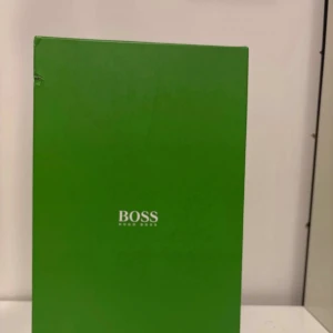 Grå sneakers från Hugo Boss strl 44 - Snygga grå sneakers från Hugo Boss med präglad textur och stilrena detaljer. Skorna har en vit sula, gröna och vita ränder på sidan samt snörning. Märket syns tydligt på sidan och sulan. Perfekta för dig som vill ha en clean och modern look.