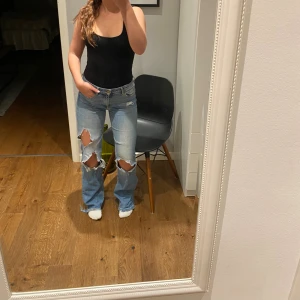 Ljusblå flare jeans från H&M, 29/34 - Säljer ett par ljusblå flare jeans från H&M i storlek 29/34. Jeansen har stora slitningar vid knäna, klassisk femficksmodell och regular waist. Tillverkade i jeansmaterial och har en snygg utsvängd passform nertill.
