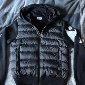  Moncler cardigan  - Svart pufferjacka från Moncler med huva och dragkedja framtill. Jackan har stickade ärmar 