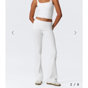 Vita bootcut yogapants med hög midja - Säljer ett par vita yogapants med bred, hög midja och bootcut-ben. Byxorna är stretchiga och sitter tajt upptill men släpper ut vid vaden. Perfekta för en chill och sportig look. Materialet är mjukt och följsamt, troligtvis polyester eller bomullsmix.