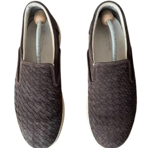 Bruna slip-on sneakers från Bottega Veneta - Snygga slip-on sneakers från Bottega Veneta i mörkbrunt flätat skinn. Skorna har en vit platt sula och klassisk rund tå. Den flätade designen ger en lyxig och unik känsla, perfekt för dig som gillar stilrena detaljer och exklusiva material.
