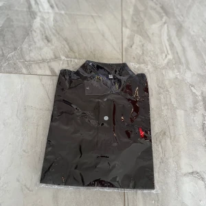 Svart piké från Polo Ralph Lauren M - Svart pikétröja från Polo Ralph Lauren i klassisk modell med krage och knappar framtill. Ikoniska röda loggan broderad på bröstet. Tillverkad i bomull för en skön och stilren känsla. Perfekt för dig som gillar enkel men snygg stil.