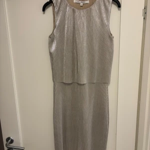 Glittrig silverklänning från KappAhl - Snygg ärmlös långklänning i glittrigt silver från KappAhl. Klänningen har en rak passform med diskreta vertikala ränder och rund halsringning. Perfekt för dig som vill sticka ut med en elegant och modern look.