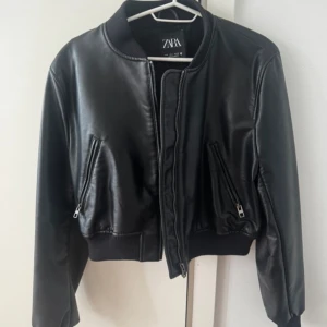 Svart bomberjacka i skinn från Zara - Snygg svart bomberjacka från Zara i skinnimitation med ribbad krage och muddar. Jackan har dragkedja framtill och två snedställda fickor med dragkedja. Perfekt för dig som vill ha en stilren och cool look. Skitsnygg till ett par jeans elr kostymbyxor på en utekväll🤍🤍