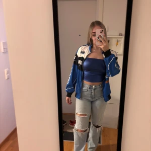 Blå racing vindjacka med tryck - Säljer en blå och svart vindjacka med vita detaljer och tryck som 'EXCITING GAME' och 'RACING'. Jackan har dragkedja framtill, ribbade muddar och sportig vibe. Oversized passform och coola prints på både fram- och baksida. Den är perfekt till sommaren då den inte är jätte tjock i materialet🫶🏻