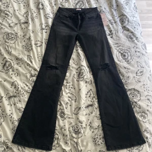 Svarta bootcut jeans från Nelly - Svarta jeans från Nelly helt oanvända med lappen på. Storlek 34 hål i knäna och med en design på bakfickorna.