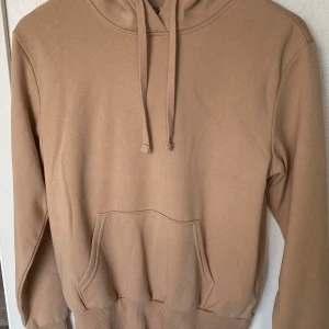 Beige hoodie från H&M Divided - En stilren beige hoodie från H&M Divided med huva och dragsko. Tröjan har en klassisk känguruficka framtill och ribbade muddar vid ärmslut och nederkant. Perfekt för en chill och avslappnad look.