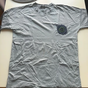 Ljusblå Moncler t-shirt med tryck - Snygg ljusblå t-shirt från Moncler med stort svart logotryck på ryggen och coolt emblem framtill med neongrön kant. T-shirten har klassisk passform och är gjord i mjuk bomull. Perfekt för dig som gillar streetstyle och vill sticka ut. (Ganska liten i storleken)