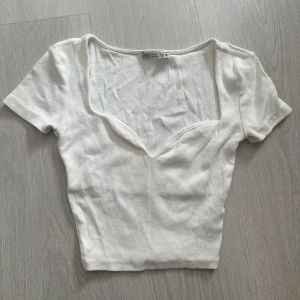Vit ribbad topp från Zara - Säljer en vit ribbad topp från Zara med korta ärmar och djup v-ringning. Toppen är croppad och har en figurnära passform. Använd fåtal gånger och i topp skick!