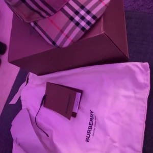 Burberry rutig keps i beige och svart - Snygg Burberry keps med klassiskt rutigt mönster i beige, svart, vitt och röda linjer. Kepsen har böjd skärm och justerbar passform. Materialet är mjukt och lätt, perfekt för dig som vill ha en ikonisk accessoar med street-vibe.