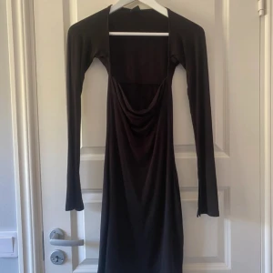 Svart långärmad klänning Gina Tricot - Svart långärmad klänning från Gina Tricot med snygg draperad urringning och figurnära passform. Klänningen är tillverkad i mjuk polyester och har långa, utsvängda ärmar. Perfekt för dig som gillar stilrena och trendiga plagg.