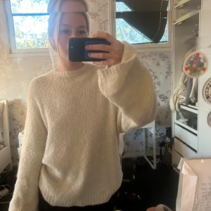 Vit fluffig stickad tröja från Wakawaka  - Supermysig fluffig stickad tröja i offwhite från Icons, storlek S. Tröjan har rund hals, långa ärmar och en loose passform. Materialet är 71% alpacka, 18% virgin wool och 11% nylon, vilket gör den extra mjuk och varm. Perfekt för kyliga dagar! Nypris 2000