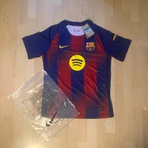 FC Barcelona Rashford 14 Nike tröja - Snygg FC Barcelona matchtröja från Nike med Rashford och nummer 14 på ryggen. Tröjan är randig i blått och rött med gula detaljer, klubbmärke och Spotify-logga på bröstet. Tillverkad i lätt och ventilerande material, perfekt för fotboll eller supporterliv.