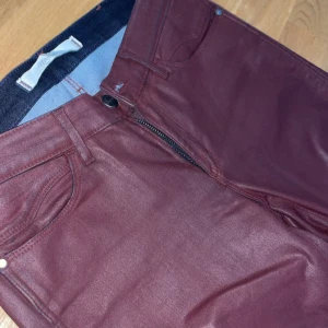 Vinröda skinny jeans från Wrangler - Snygga vinröda skinny jeans från Dr. Denim med glansig finish. Klassisk femficksmodell, dragkedja och knapp framtill. Jeansen har bälteshällor och är tillverkade i ett stretchigt material som sitter tajt och bekvämt.