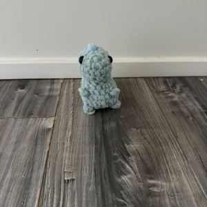 Virkad dinosaur  - En söt, handgjord virkad dinosaurie i ljusblått och mint garn med svans och svarta ögon. Perfekt som present eller dekoration.