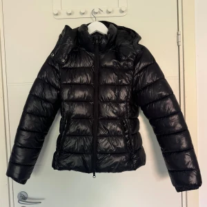 Svart pufferjacka  - Säljer en svart glansig pufferjacka från lager 157. Fint skick och knappt använd. Storlek XS