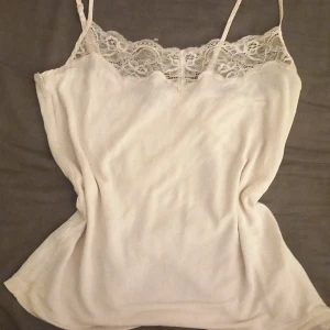 Vit spetslinnetopp från Twilfit - Supersöt beige linnetopp från Twilfit med tunna axelband och super fina spetsdetalj upptill. Toppen är i ett mjukt och lätt material som känns skönt mot huden. Ett perfekt natt linne.