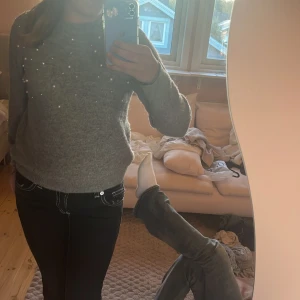 Grå stickad tröja med pärlor - Supermysig grå stickad tröja från Kappahl med pärldetaljer framtill. Tröjan har rund halsringning, långa ärmar och ribbade muddar. Perfekt för kyliga dagar och ger en snygg touch till din outfit.