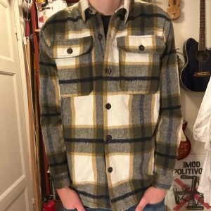 Rutig overshirt från Zara i ullmix - Overshirt från Zara i mjuk ullmix med rutigt mönster i beige, grått och olivgrönt. Klassisk krage, två bröstfickor med knappar och långa ärmar. Perfekt lager-på-lager-plagg med snygg passform och snygga detaljer.