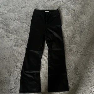 Svarta bootcut byxor från VILA - Snygga svarta byxor från VILA med bootcut-modell och glansig finish. Byxorna har klassisk femficksdesign, dragkedja och knapp framtill. Materialet har en skinnliknande känsla som ger en cool look. Perfekta för dig som vill sticka ut lite extra.