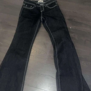 Mörka bootcut jeans med kontrastsömmar - Snygga mörkblå jeans med tydliga vita kontrastsömmar och bootcut-modell. Klassisk femficksdesign och låg midja. Perfekta för dig som gillar en retrovibe och vill sticka ut lite extra med detaljerna.