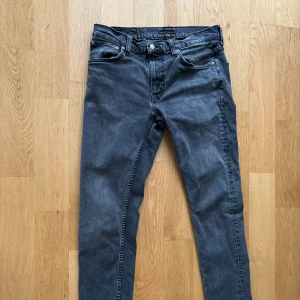 Grå jeans från Nudie Jeans - Snygga grå jeans från Nudie Jeans med svarta broderade detaljer på bakfickorna. Modellen är Lean Dean i stl W32 L34.