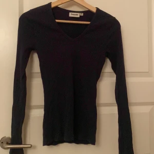 Svart ribbad långärmad topp Kappahl - En marinblå långärmad topp från Kappahl i storlek XS. Toppen har v-ringning och är ribbad för en snygg och figurnära passform. Perfekt att styla med jeans eller kjol för en enkel och clean look. 