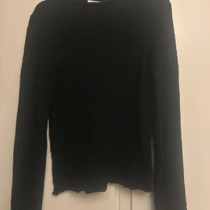 Svart stickad spets långärmad tröja - Mysig svart stickad tröja med lång ärm och diskret strukturmönster. Tröjan har en enkel rund halsringning och en något vågig nederkant som ger en avslappnad vibe. Perfekt för lager-på-lager under kyliga dagar.