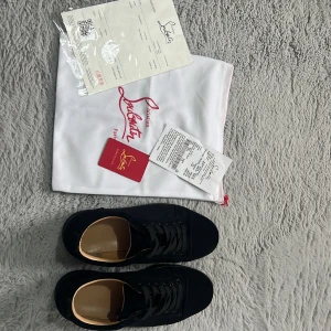 Svarta sneakers från Christian Louboutin - Snygga svarta sneakers från Christian Louboutin med klassisk röd sula och diskret logga. Skorna har rund tå, snörning och är tillverkade i skinn och textil. Perfekta för dig som vill ha en lyxig och stilren look med en ikonisk touch.