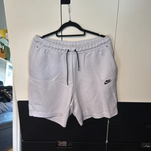 Nike tech fleece shorts - Snygga vita shorts från Nike med elastisk midja och svart snörning. Klassisk Nike-logga på ena benet och praktiska fickor, varav en med dragkedja bak. Perfekta för träning eller chill dagar. Mjukt material som känns skönt mot huden. Aldrig använda säljer då dom är för stora för mig.
