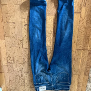 Blå jeans från Jacob Cohen med slitning - Snygga blå jeans från Jacob Cohen med slitna detaljer och hål på ena benet. Modellen har klassisk femficksdesign, knappgylf och smal passform. Jeansen har en cool tvätt med ljusare partier och är perfekta för en avslappnad streetstil.