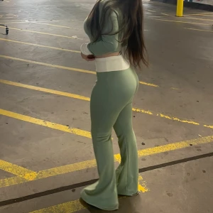 Gröna bootcut byxor med hög midja - Snygga ljusgröna bootcut byxor med matchande tröja till som har en dragkedja. Byxorna har en tight passform upptill och vida ben nertill, vilket ger en trendig siluett. Det är jätte fin sätt för ha när man ska gå ut eller bara vara hemma den är ljusgrön och vita detaljer. Har använt den väldigt få gången alltså mindre än 5 gånger 