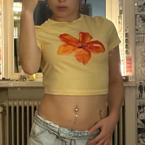 Gul croppad topp med orange blomma - Säljer en ljusgul croppad topp med korta ärmar och en stor orange blomma tryckt framtill. passar xs, från shein och är aldrig använd