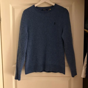 Blå stickad tröja Polo Ralph Lauren - Säljer en blå stickad tröja från Polo Ralph Lauren i storlek M. Tröjan är en blandning av ull och bomull. Stilren och i mycket fint skick, har använts 3 gånger och väldigt sparsamt 
