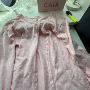 Ljusrosa kofta från Soya Concept - Supersöt ljusrosa kofta från Soya Concept med rund halsringning och knappar hela vägen framtill. Långärmad och i mjuk, tunn stickad bomullsmix som passar perfekt till lager på lager. Enkel och stilren design som är lätt att matcha. Ärm= 58cm Längd=55cm jag skulle säga att den är xs/s