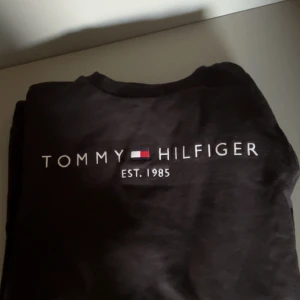 Svart långärmad tröja Tommy Hilfiger - Svart långärmad tröja från Tommy Hilfiger med broderad logga och texten 'EST. 1985' på bröstet. Klassisk crewneck-modell i mjuk bomull, perfekt för en clean och stilren look.Köpt för 800kr på NK och sen dess bara legat och samlat damm.Skulle behöva tvättas men har inte gjort det för hade inte tänkt sälja den.för mer frågor och funderingar kontakta mig😁