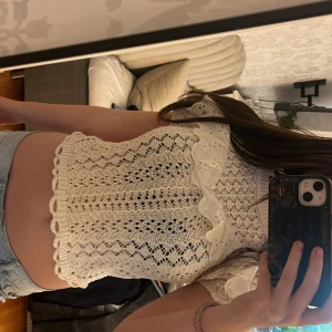 Vit topp med volang från Zara - Supersöt vit topp från Zara med korta ärmar och broderad volangdetalj över bröstet. Blusen har ett genombrutet mönster och ribbad halsringning. Perfekt till jeans eller kjol för en romantisk vibe.