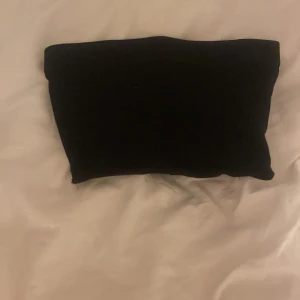 Svart bandeau tubtopp från H&M Divided - En svart bandeau tubtopp från H&M Divided i storlek XS. Enkel och stilren design utan axelband, perfekt att matcha med höga jeans eller kjol. Gjord i mjukt stretchigt material för en bekväm passform.