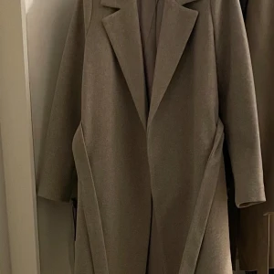 Beige kappa från ONLY med bälte - Säljer en stilren vadlång beige höst kappa från ONLY i storlek M. Kappan har klassisk krage, långa ärmar och ett bälte i midjan för snygg passform. 