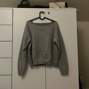 Grå offshoulder stickad tröja - Säljer en grå stickad tröja med offshoulder-modell och långa ärmar. Tröjan har en avslappnad passform och ribbade muddar vid ärmslut och nederkant. Perfekt för lager-på-lager och chill dagar. Oversized.