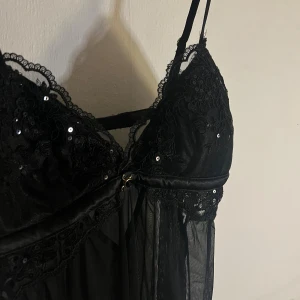 Svart spets nattlinne/topp med paljetter - Säljer ett svart nattlinne/topp med tunna axelband med inbyggd bh. Der är spetsdetaljer och små paljetter på bysten. Den har mesh nertilll. 😘💞Köpt på new yourker och använt max tre gånger. 