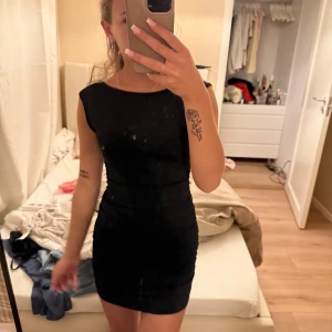 Svart tight kortklänning med öppen rygg - Säljer en svart tight kortklänning med öppen rygg och knytband i nacken. Klänningen har ärmlös design och en enkel, stilren look som framhäver figuren. Perfekt för dig som gillar minimalistisk stil med en twist.